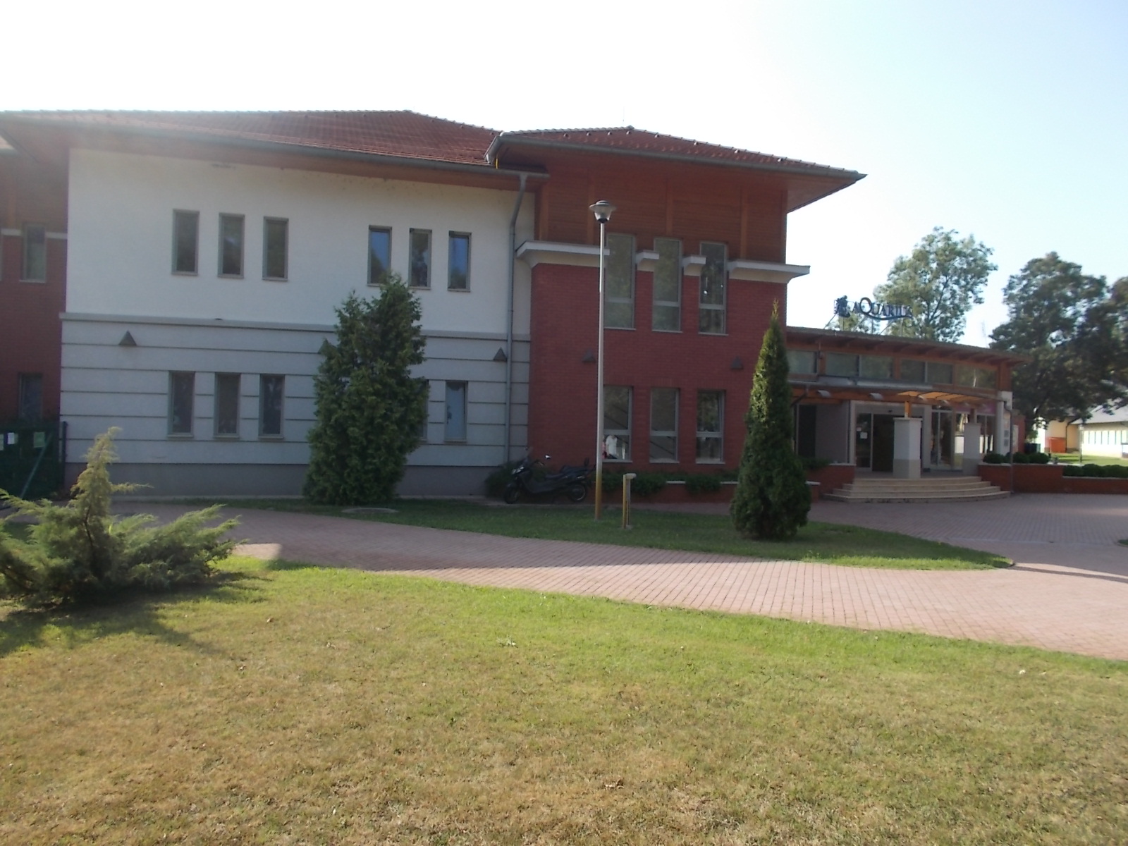 Exterior of the Aquarius Spa complex in Sóstógyógyfürdő, Nyíregyháza, with its red-brick and white facade and the Aquarius sign above the entrance