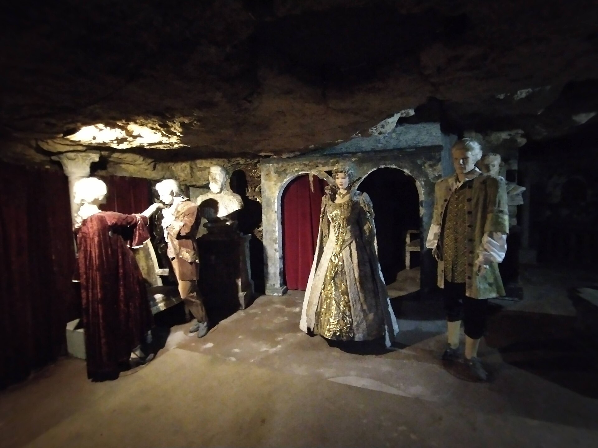 Costumed mannequins in period dress standing in a dimly lit cave chamber of the Labyrinth of Buda Castle