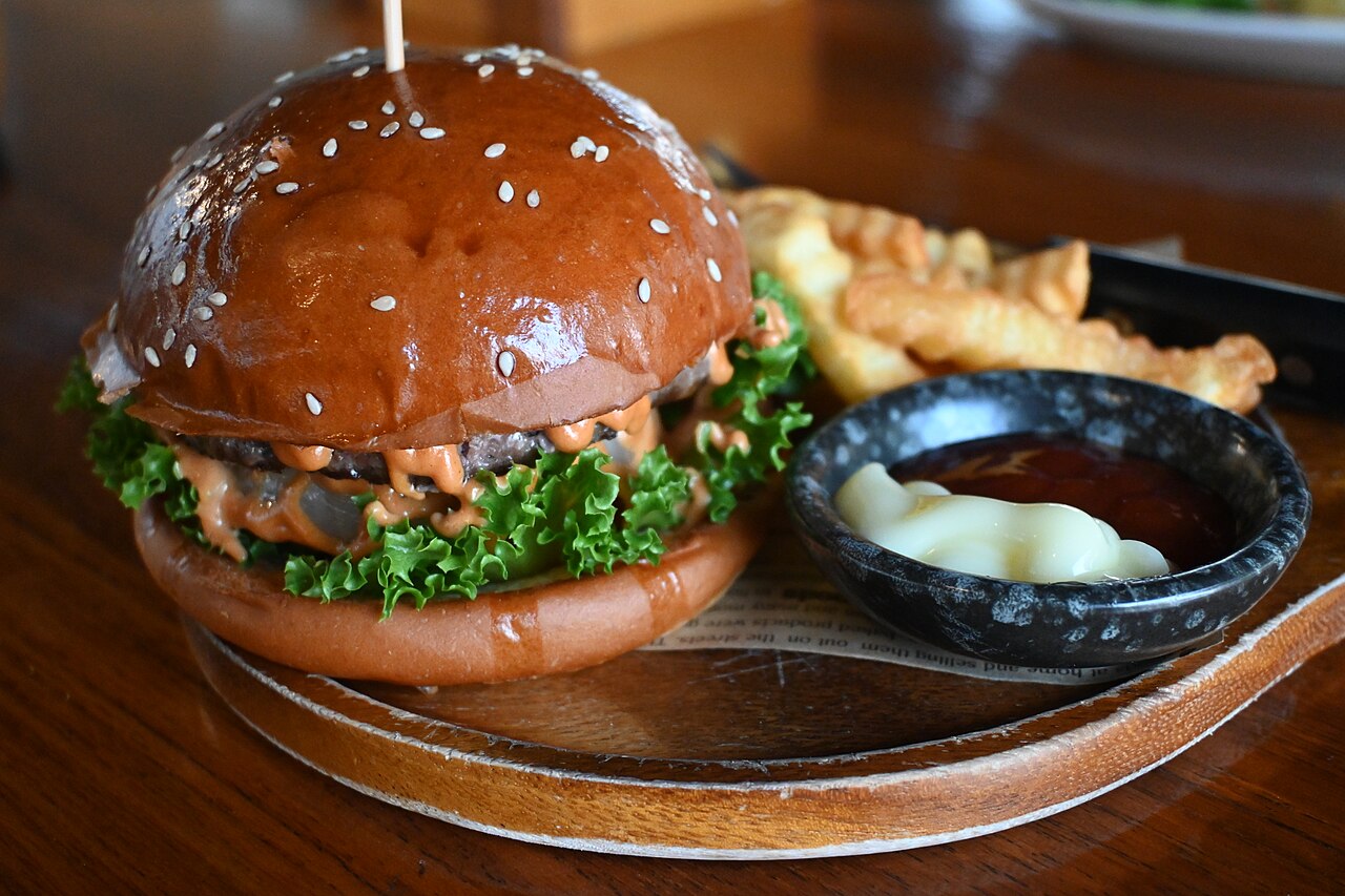 A stacked gourmet burger with fries on a wooden board