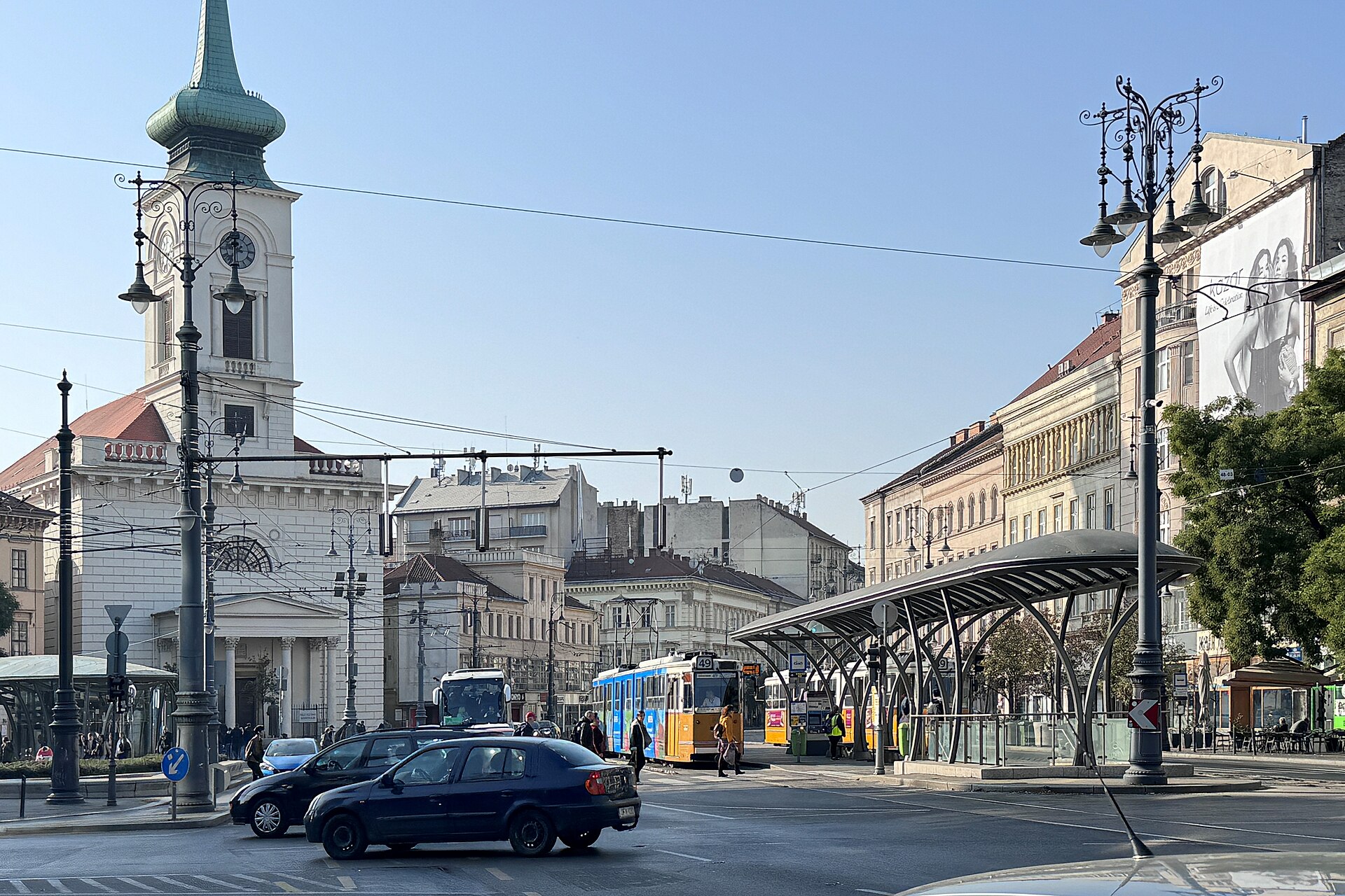 Kálvin tér in Budapest with the white Reformed church tower, a yellow tram at the stop and traffic crossing the square.