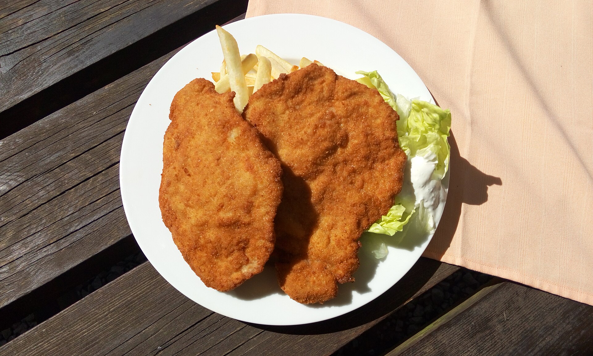 Two golden breaded pork cutlets on a white plate with french fries and shredded lettuce, the classic Hungarian rántott hús.