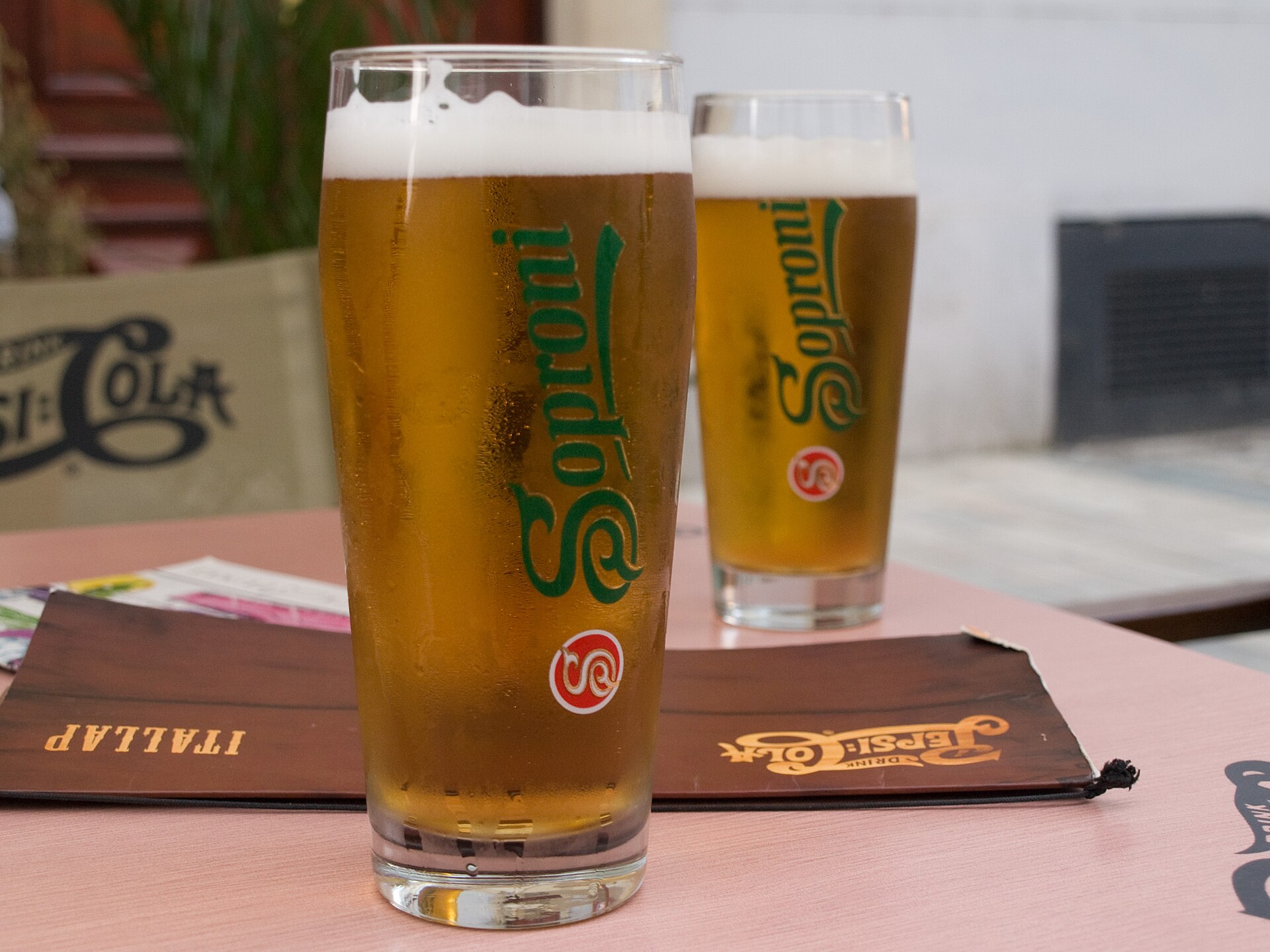 Two branded glasses of Soproni lager standing on a pub table