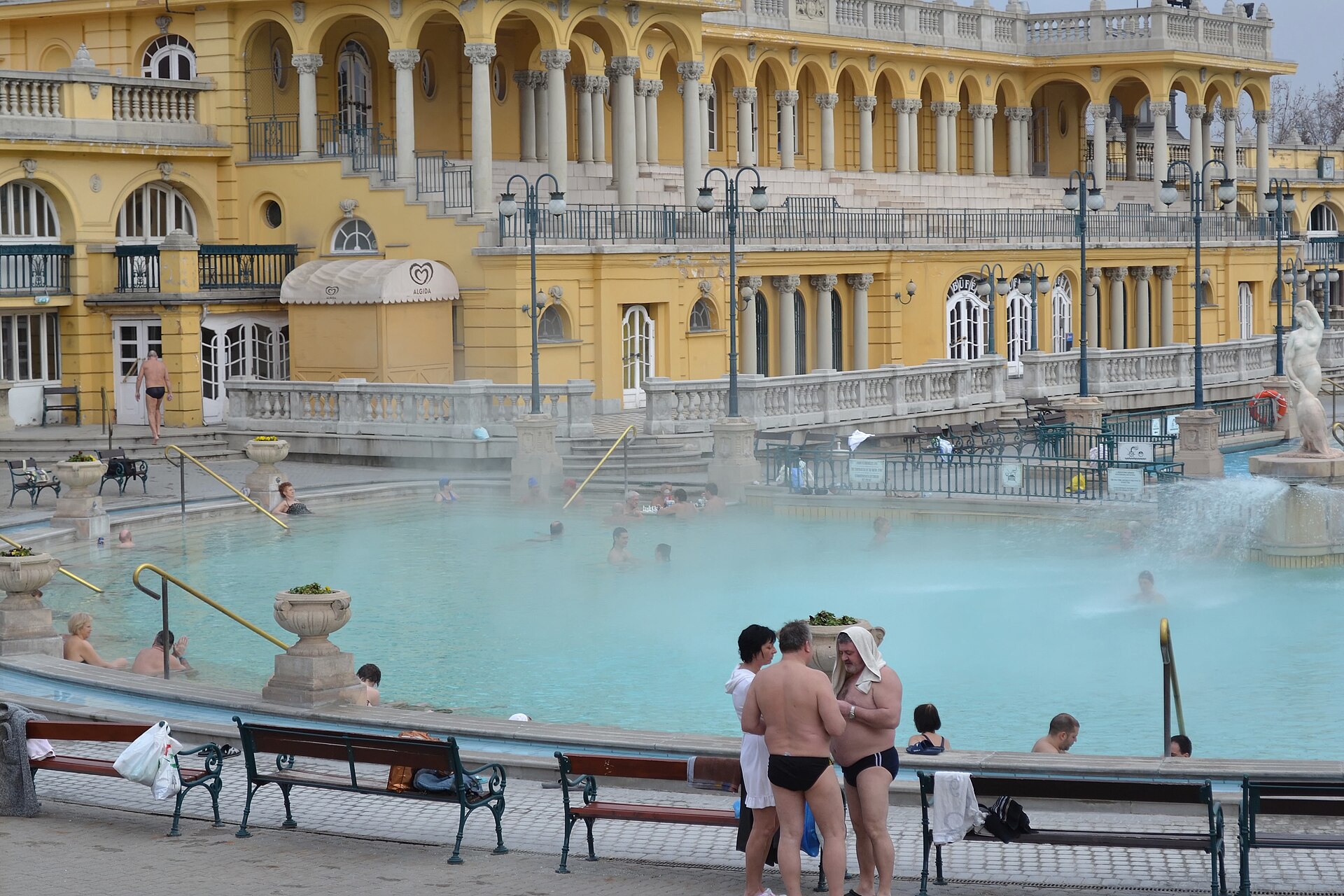 Bagnanti nella vasca termale esterna fumante delle Terme Széchenyi a Budapest, davanti all’edificio termale giallo neo-barocco