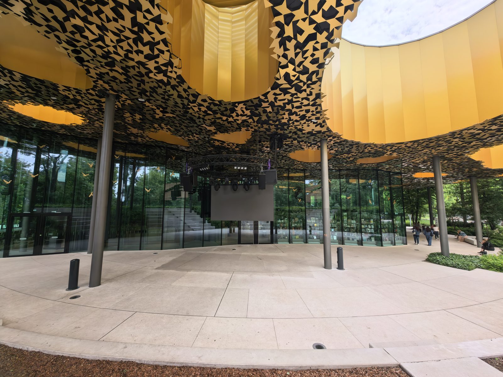 The perforated golden canopy of the House of Music Hungary from below, with the glass walls and City Park trees behind
