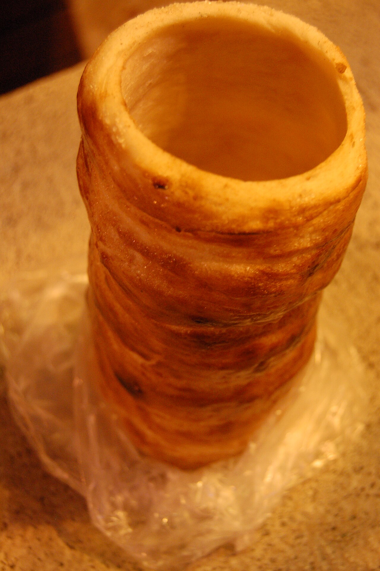 A single kürtőskalács standing on end, its spiral of caramelised sugar-crusted dough wound around a hollow centre.