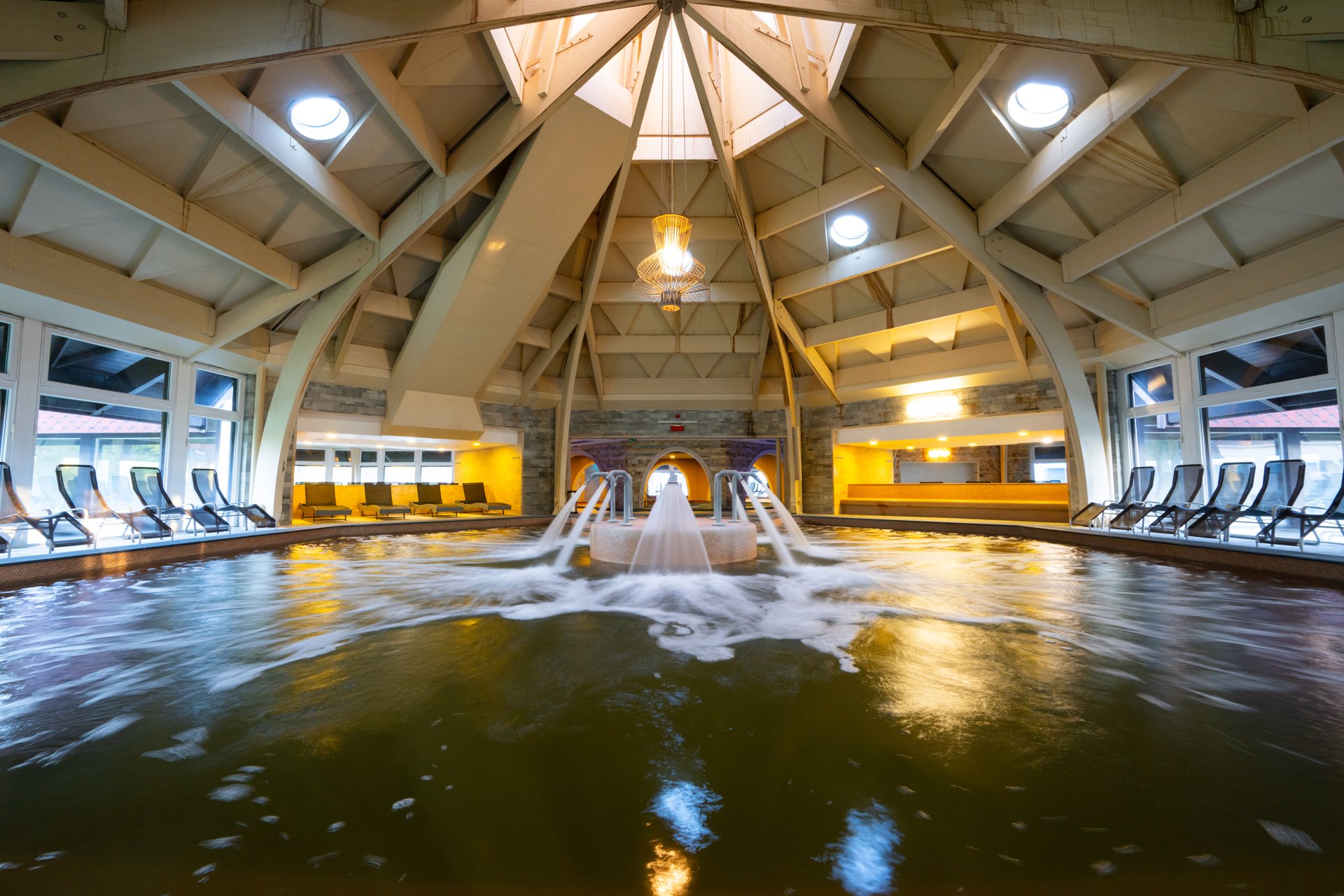 The thermal hall at Aquaticum Debrecen: water jets pouring into a pool under the domed timber ceiling