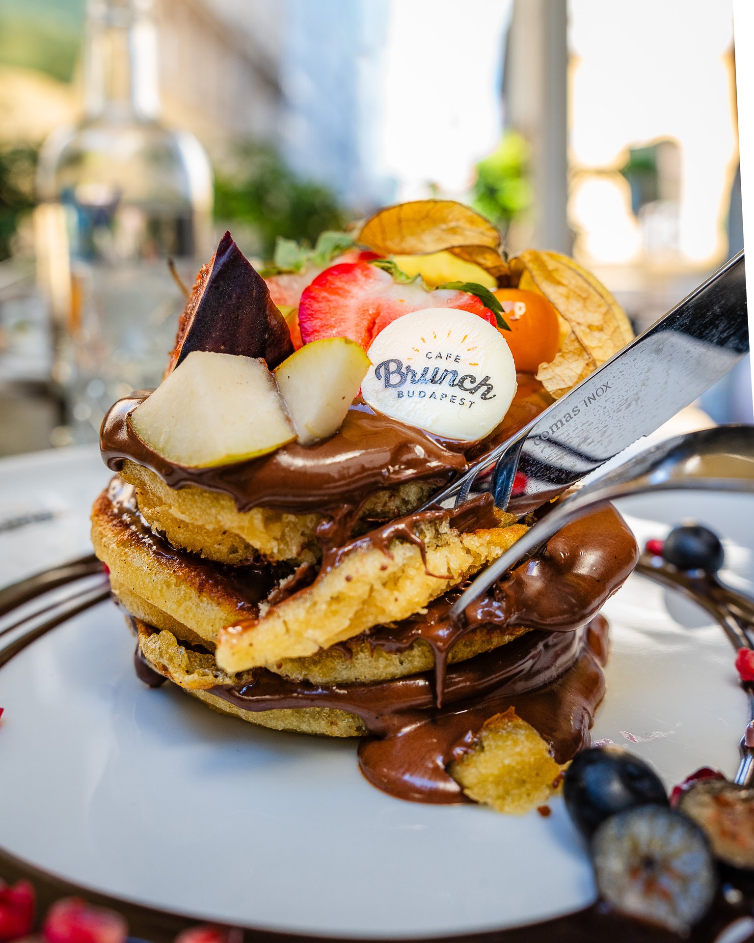 Una torre di pancake sotto la salsa al cioccolato da Cafe Brunch Budapest, frutta e la bandierina della casa sopra