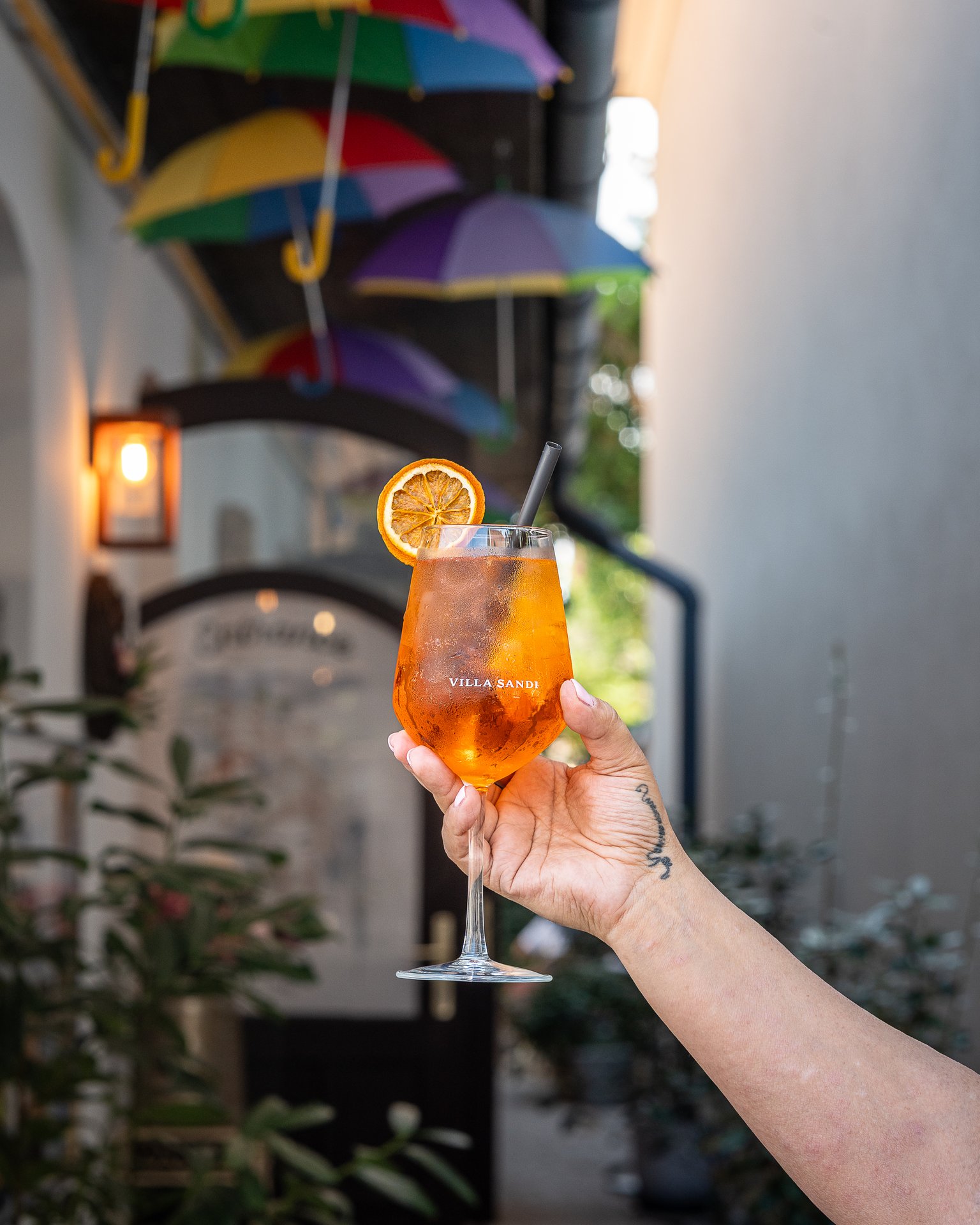 Aperol Spritz held up under a canopy of umbrellas at Cafe Brunch Szentendre