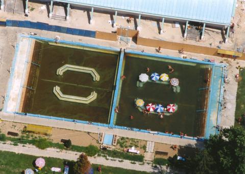 מבט אווירי מקרוב על שתי בריכות חיצוניות מלבניות במרחצאות איגאל, עם מתרחצים ושמשיות