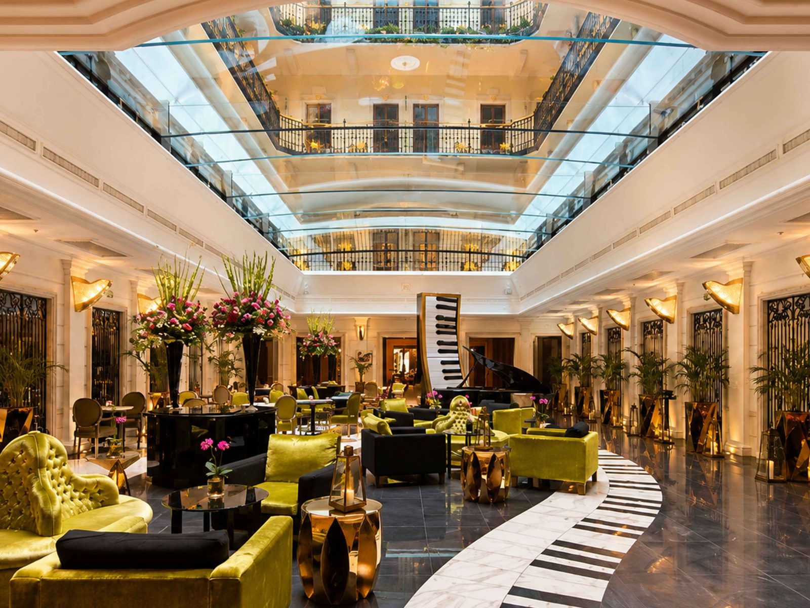 The glass-roofed atrium of the Aria Hotel Budapest, with lime-green velvet armchairs, a grand piano and a black-and-white path shaped like piano keys running across the marble floor