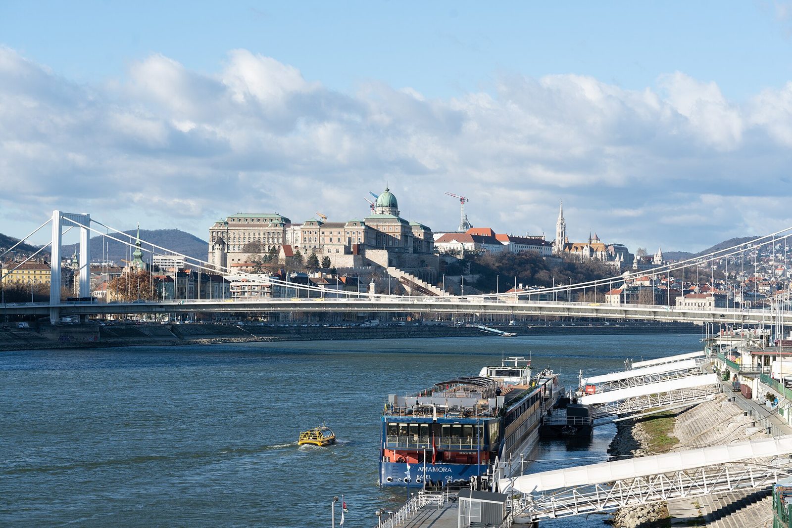 The Royal Palace of Buda Castle with its green dome on Castle Hill, seen across the Danube with the Elisabeth Bridge in front and a river cruise ship moored on the Pest bank
