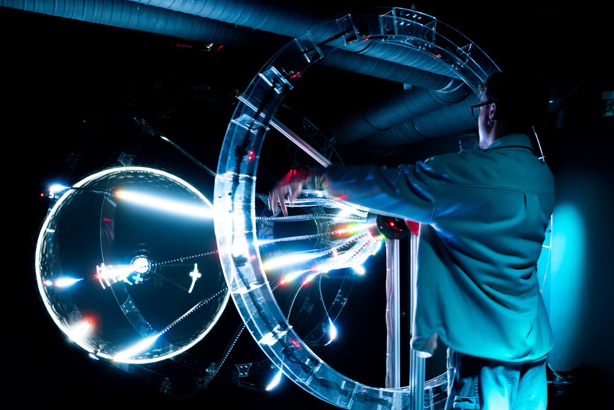 A visitor reaching into large transparent rings lit with LED strips at Cinema Mystica