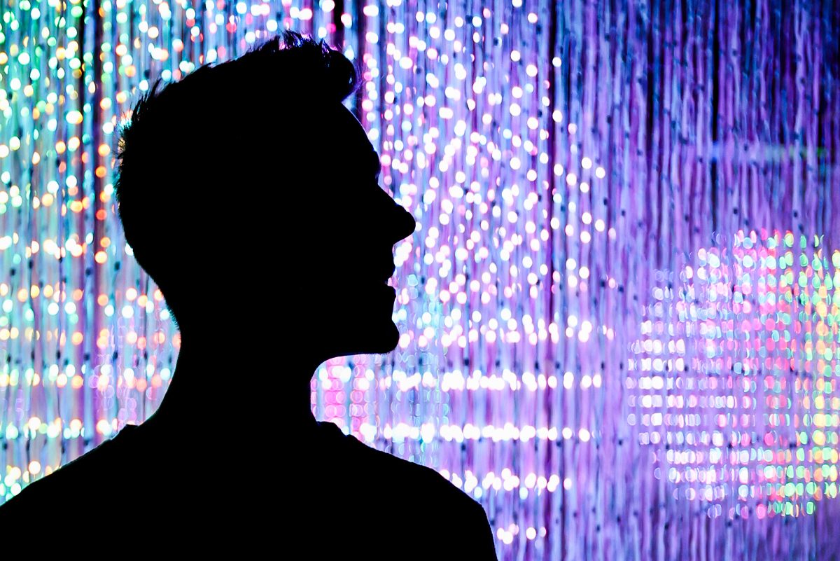 A visitor’s silhouette in profile against a curtain of colored lights at Cinema Mystica