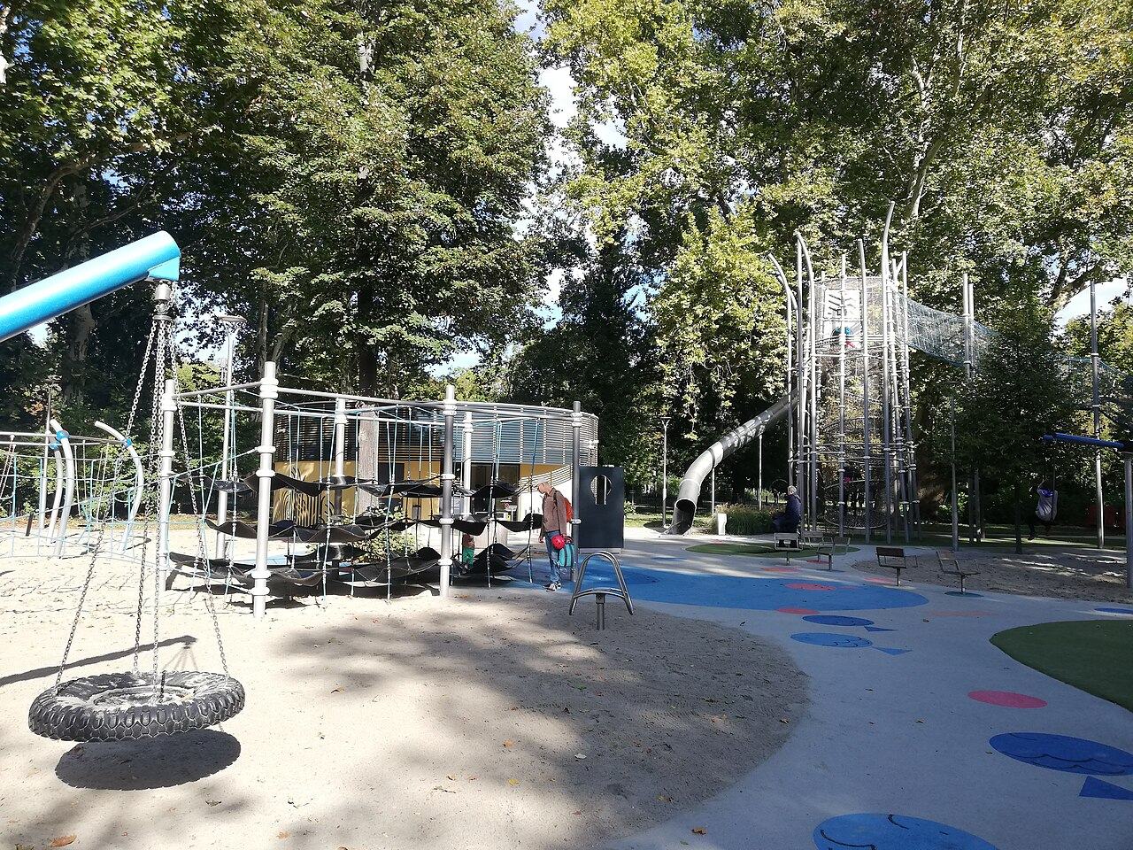 A nest swing, a rope climbing frame and a slide tower under the trees at the City Park Main Playground