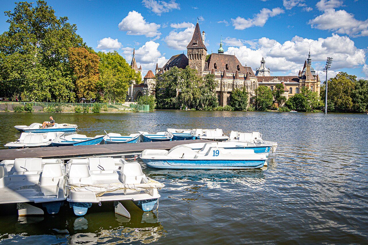 Pedal boats moored at a jetty on the City Park lake, with Vajdahunyad Castle rising behind the trees