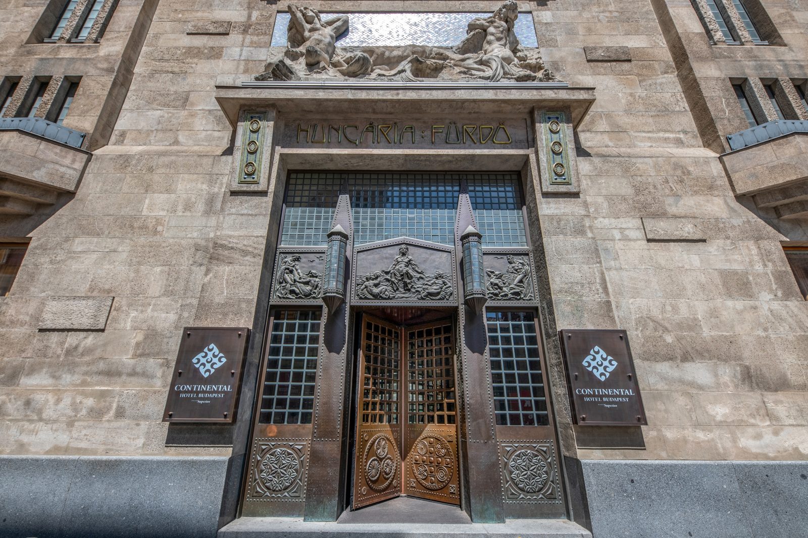The stone entrance of the Continental Hotel on Dohány utca, with the old Hungária Fürdő lettering and a carved relief above the doors