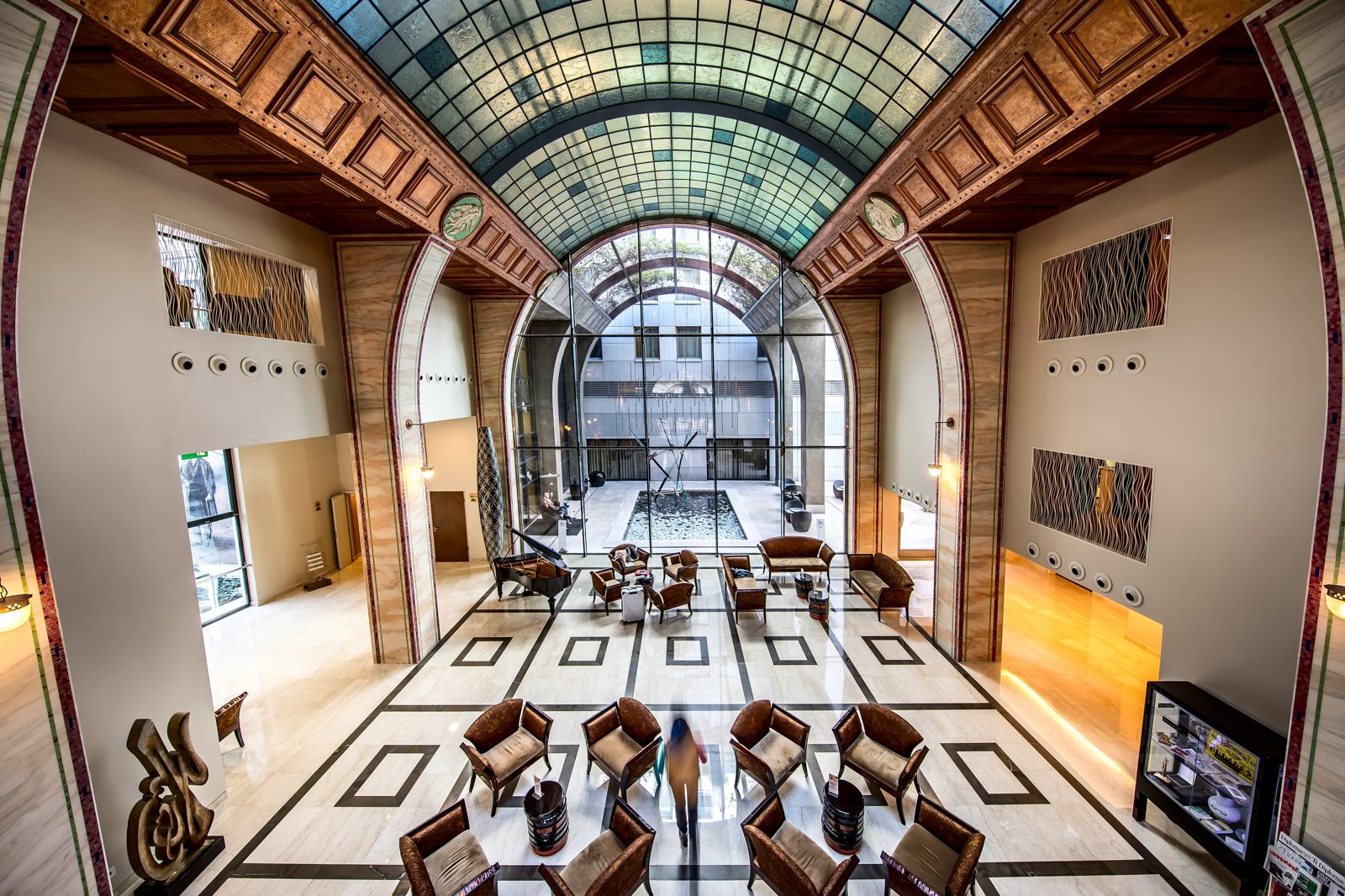 The Continental Hotel’s lobby under a long arched glass roof, with armchairs on a patterned marble floor