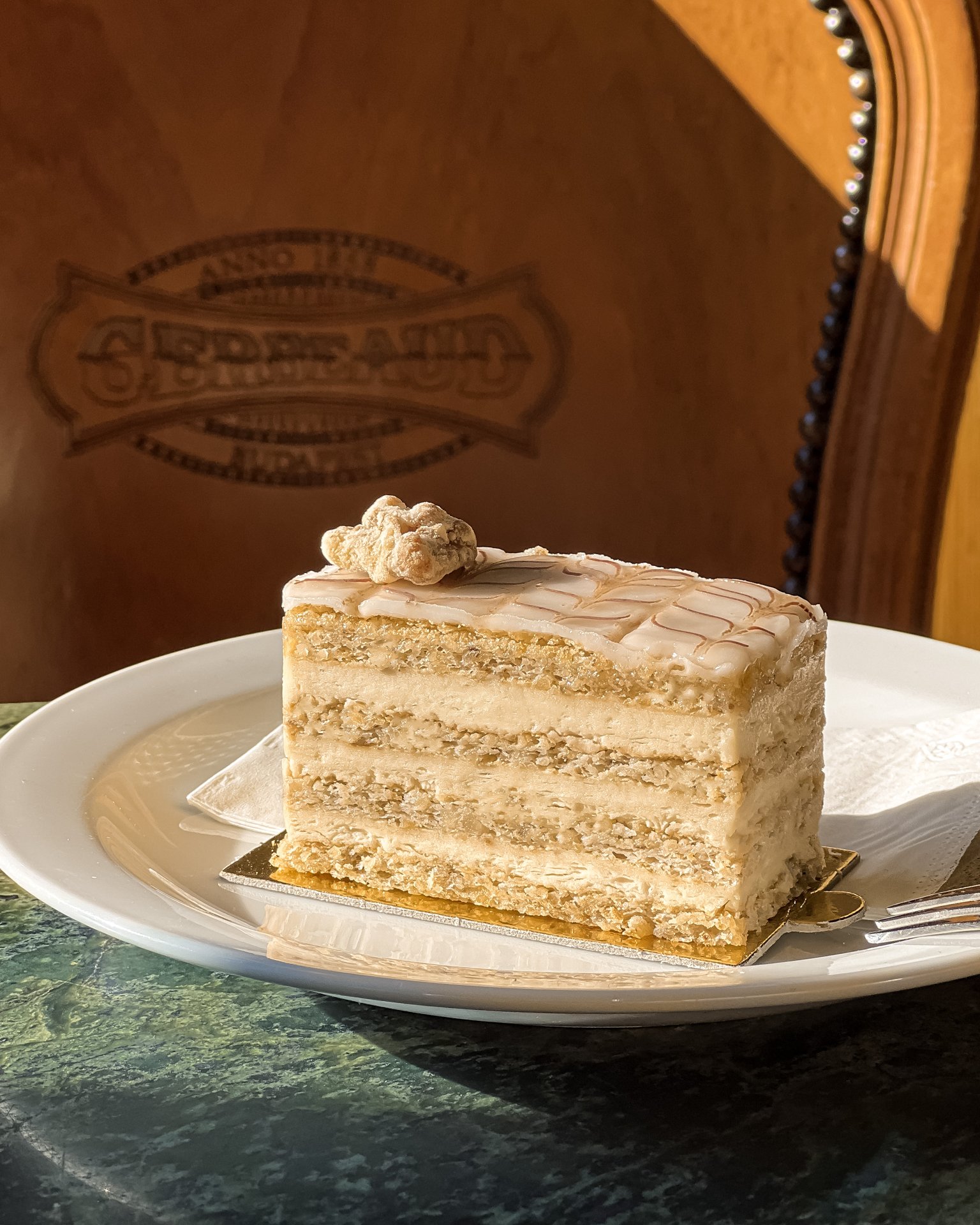 Una fetta Esterházy del Café Gerbeaud, con la glassa bianca e la ragnatela di cioccolato, su un piatto a un tavolo di marmo