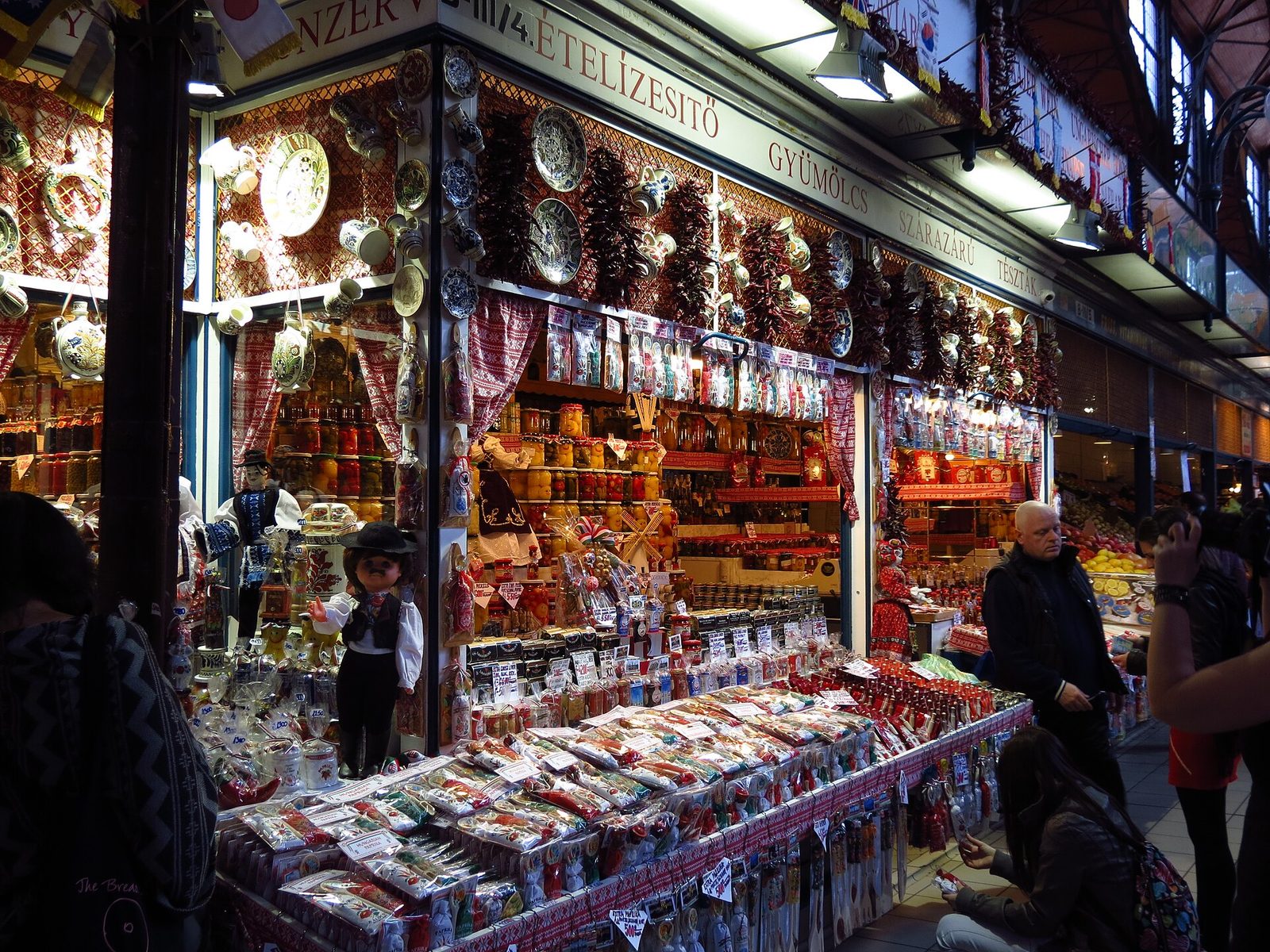 A ground-floor stall at the Great Market Hall with painted ceramics hanging among strings of dried red peppers, jars of preserves on the shelves and bags of paprika on the front counter