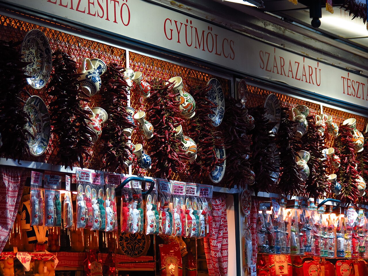 Strings of dried red peppers and painted ceramic jugs and plates hanging over a stall at the Great Market Hall, with bags of paprika hanging from a rail below