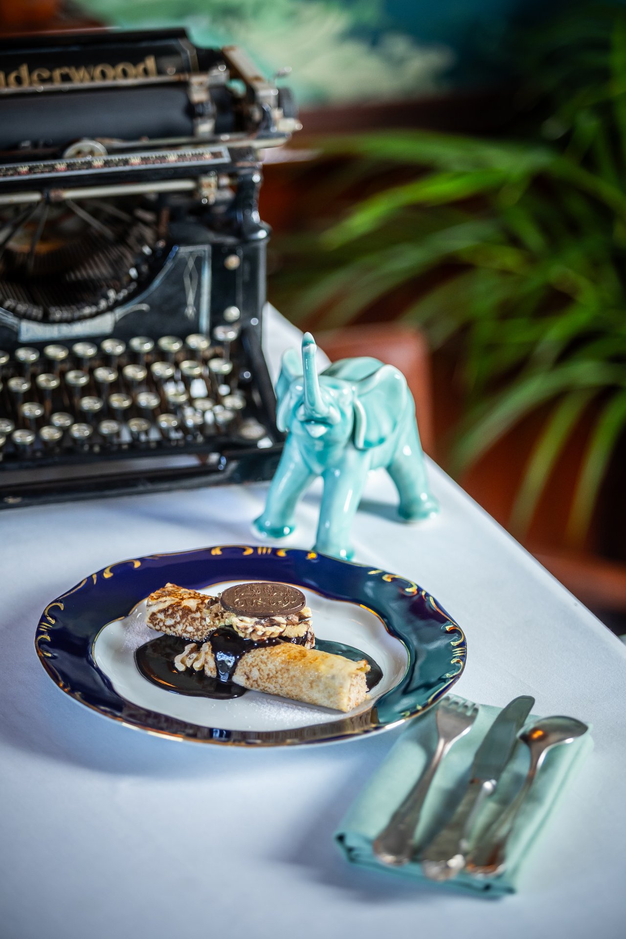 The Gundel pancake with walnut filling and chocolate sauce on a blue and gold plate, an old typewriter behind it