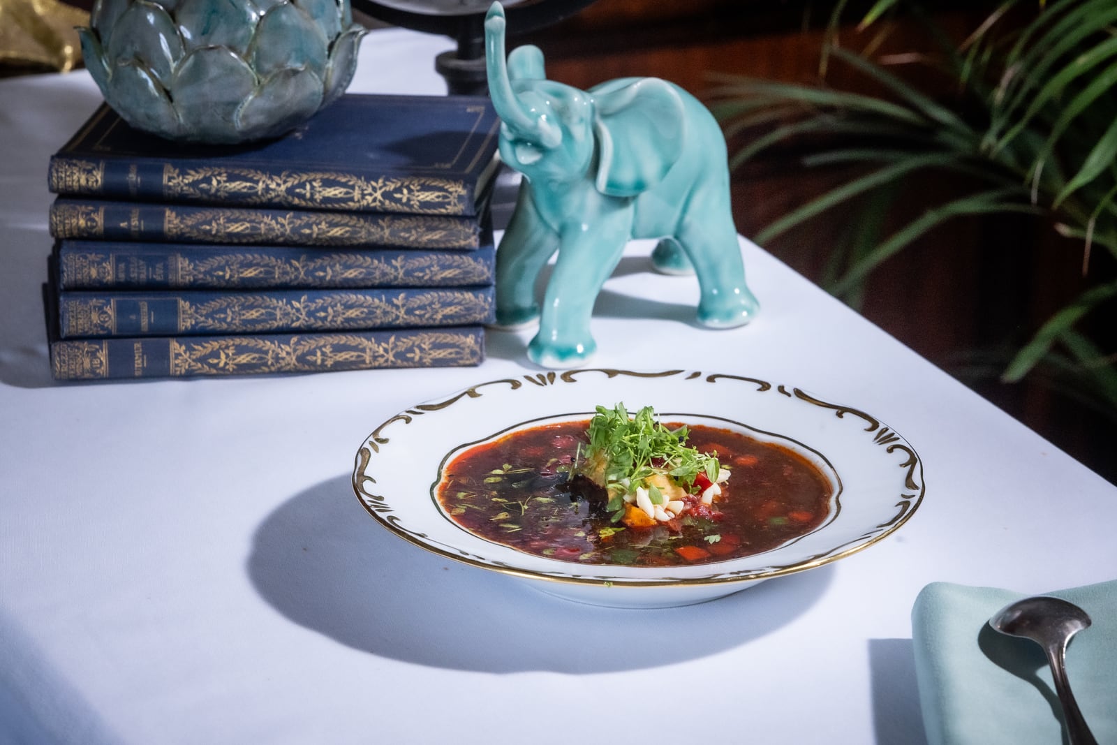 Gundel goulash soup in a white and gold bowl, with a turquoise elephant and stacked books behind it