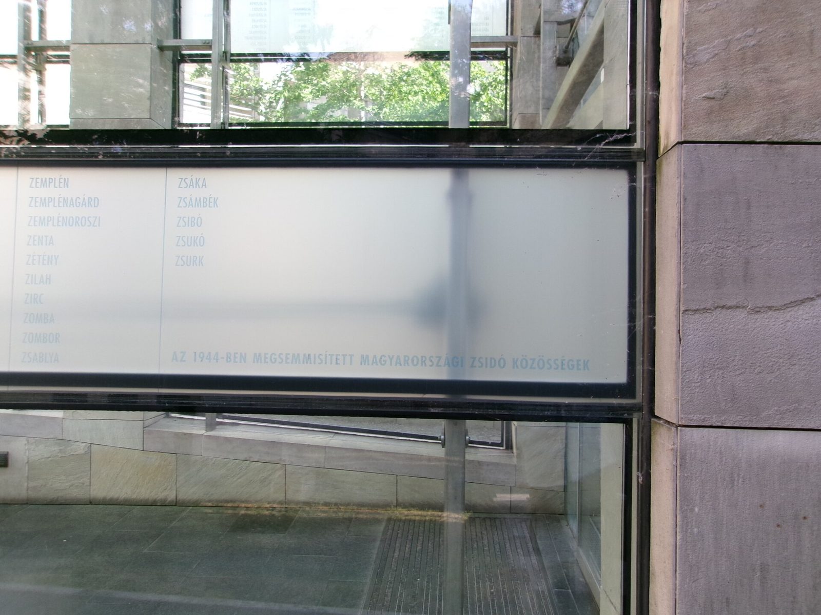 A frosted glass pane of the Tower of Lost Communities listing Hungarian towns from Zemplén to Zsurk under the line naming the Jewish communities destroyed in 1944