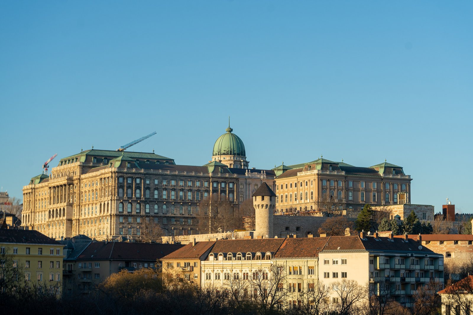 L’ancien Palais royal sur la colline du Château de Buda, ses longues ailes en pierre claire et sa coupole verte éclairées par un soleil d’hiver rasant, au-dessus des toits des quais de Buda