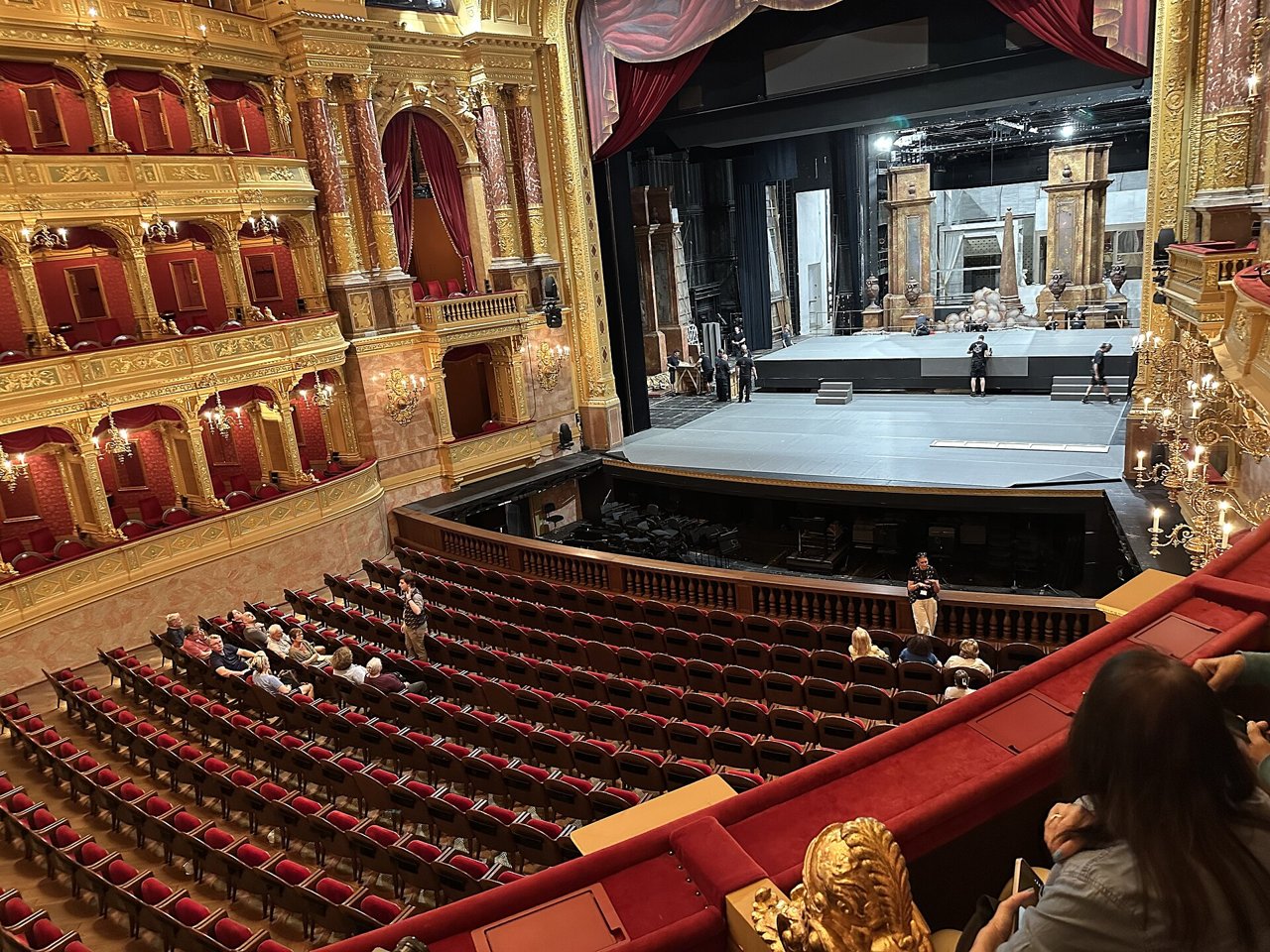 The auditorium of the Hungarian State Opera House seen from a box during a daytime tour, with a stage crew setting up, photographed in 2026