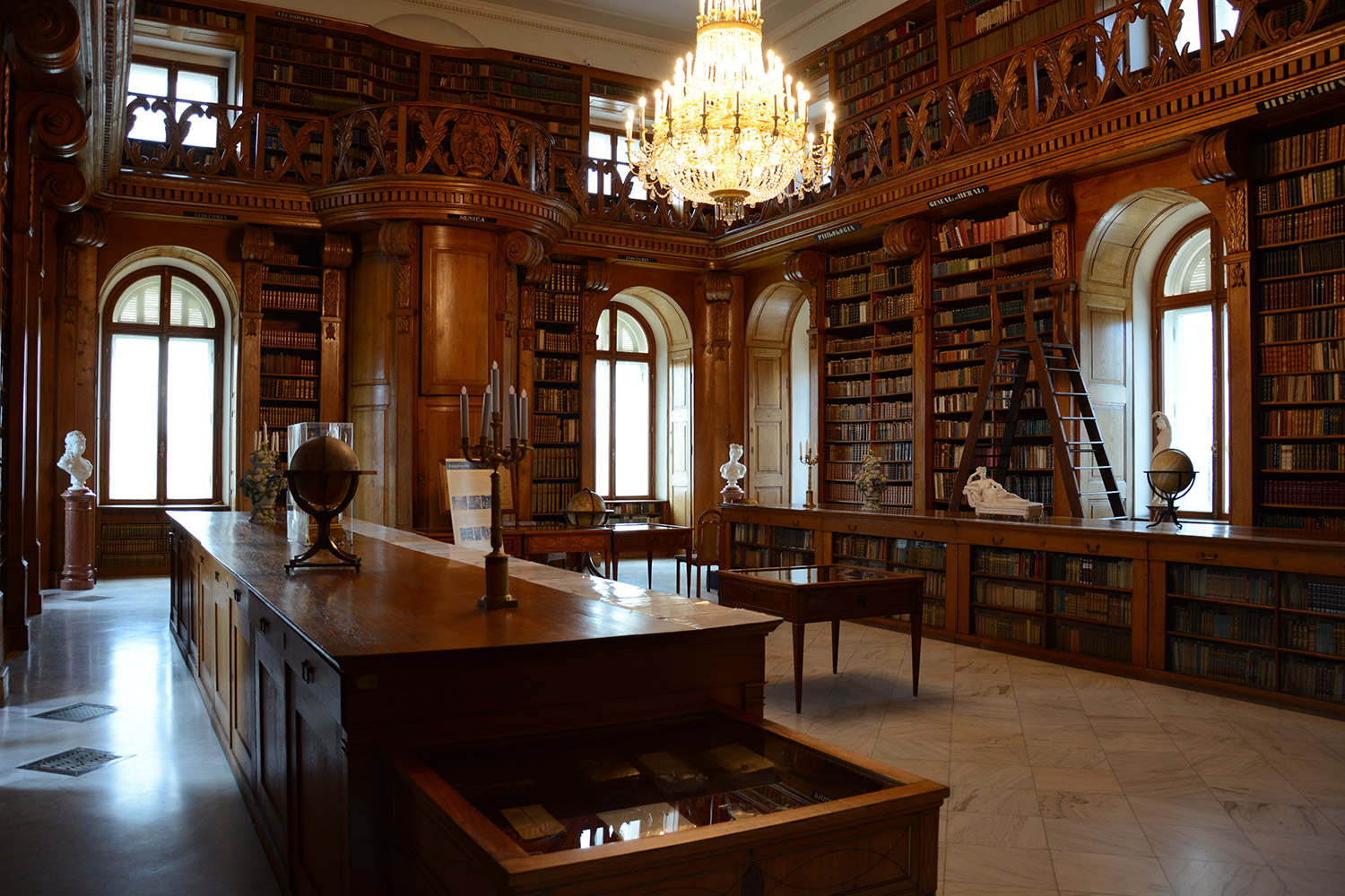 The Helikon Library in the Festetics Palace, with floor-to-ceiling oak bookcases, a gallery and a crystal chandelier above a long reading table
