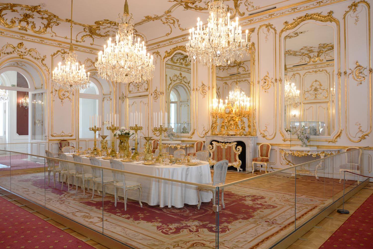 A white and gilded hall in the Festetics Palace with crystal chandeliers, tall mirrors and a long table laid for a banquet