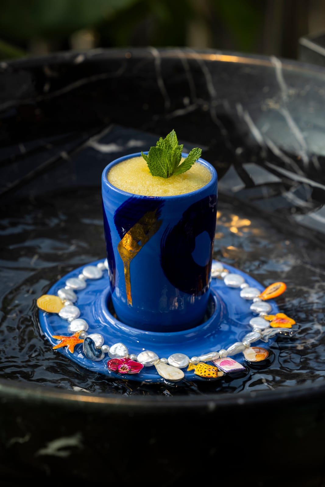 A frozen yellow cocktail with a mint sprig in a blue ceramic cup at Leo Rooftop
