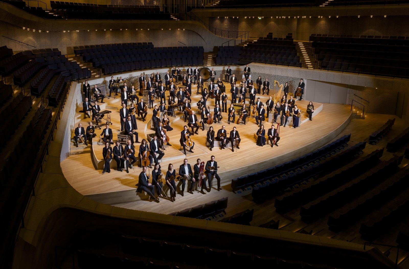 The NDR Elbphilharmonie Orchestra posing with their instruments on the stage of the Elbphilharmonie's Grand Hall in Hamburg, empty seats rising around them