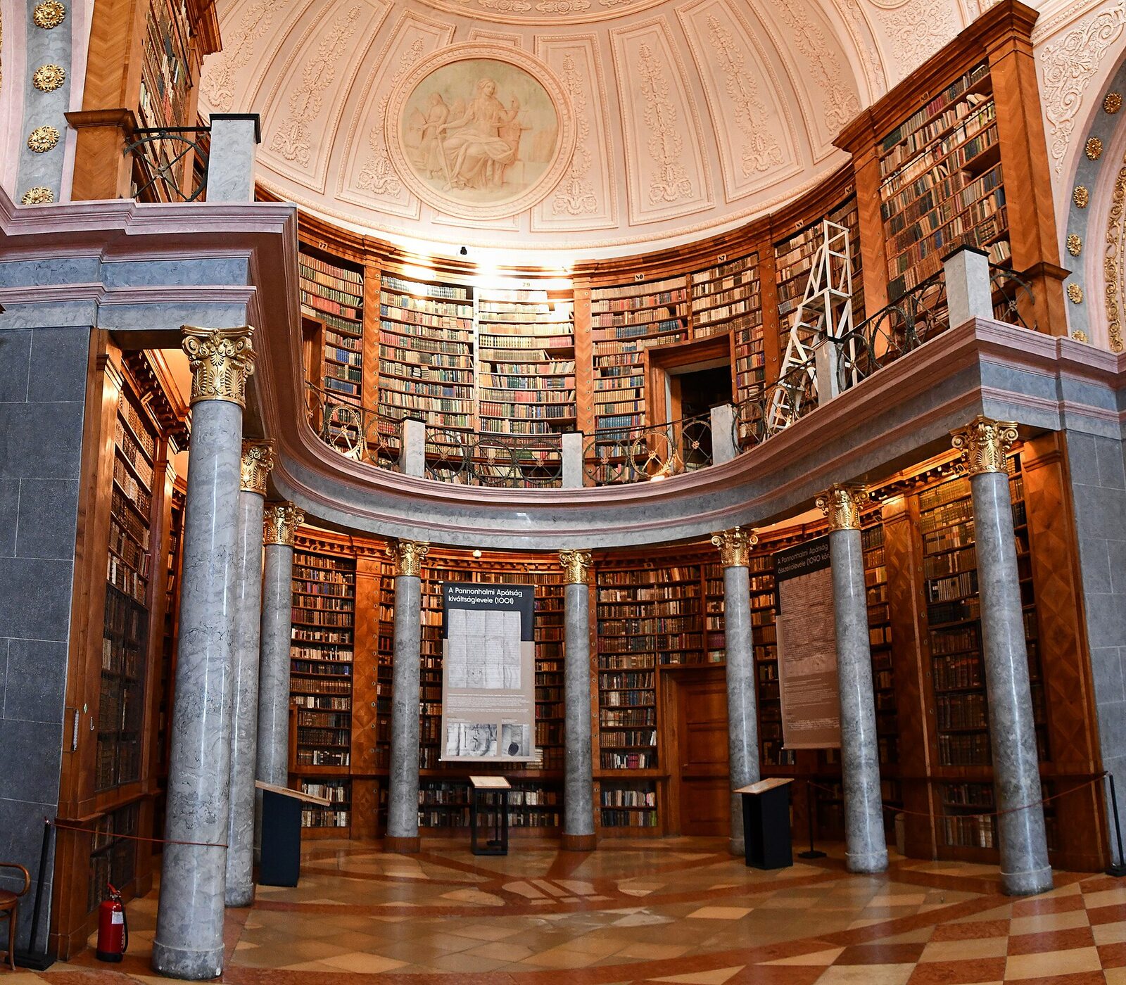 The oval main hall of the Pannonhalma Archabbey library, with tall wooden bookcases, marble columns and a painted ceiling