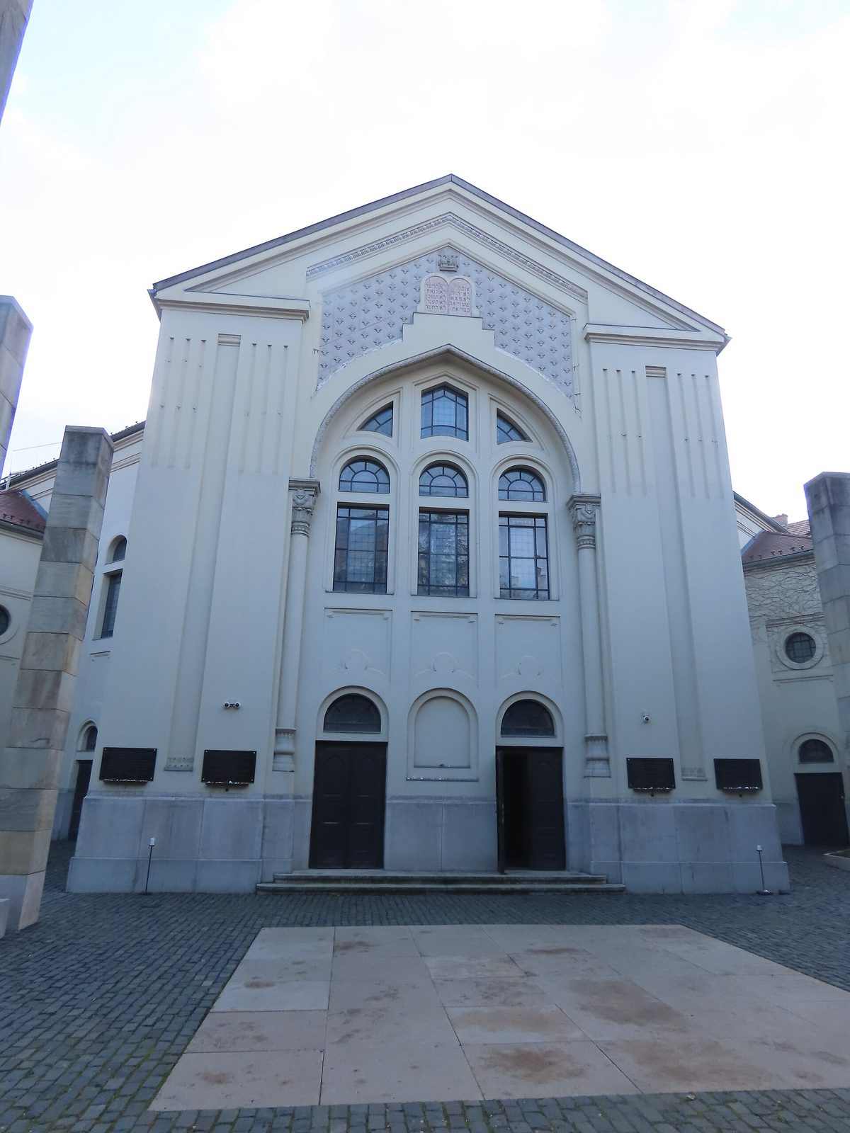 The pale restored facade of the Páva Street synagogue in Budapest, with its large arched window and twin doors