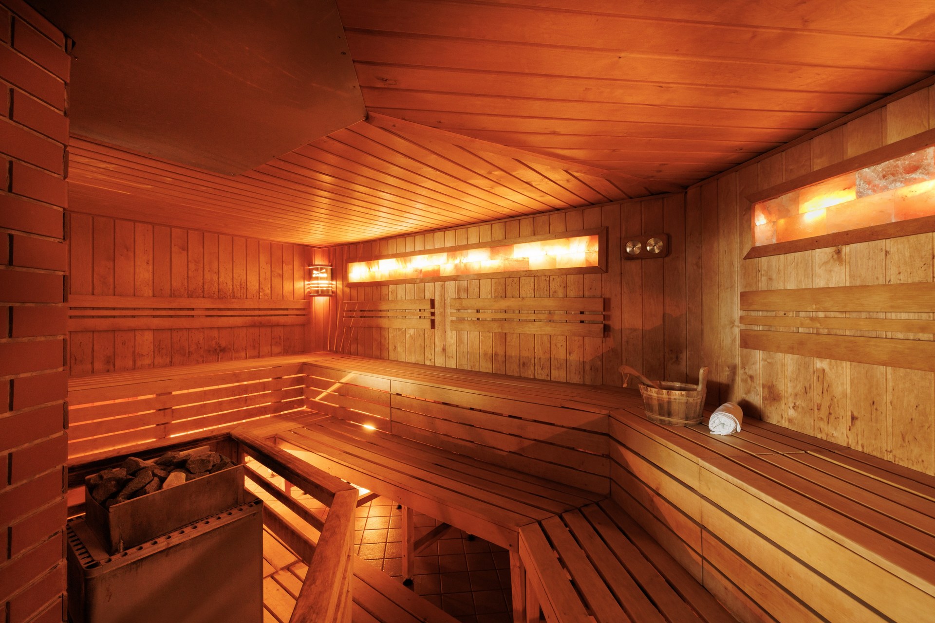 Una sauna in legno vuota a Sárvár, con panche a gradoni, una stufa con le pietre e pannelli ambrati illuminati nelle pareti