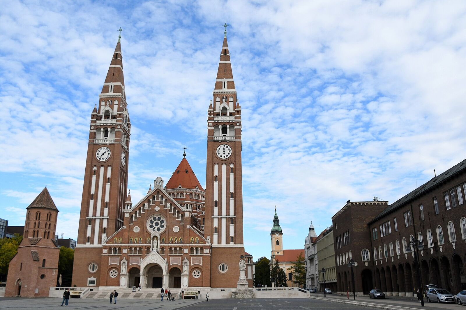 The twin brick towers of the Votive Church rising over Dóm tér in Szeged under a blue sky
