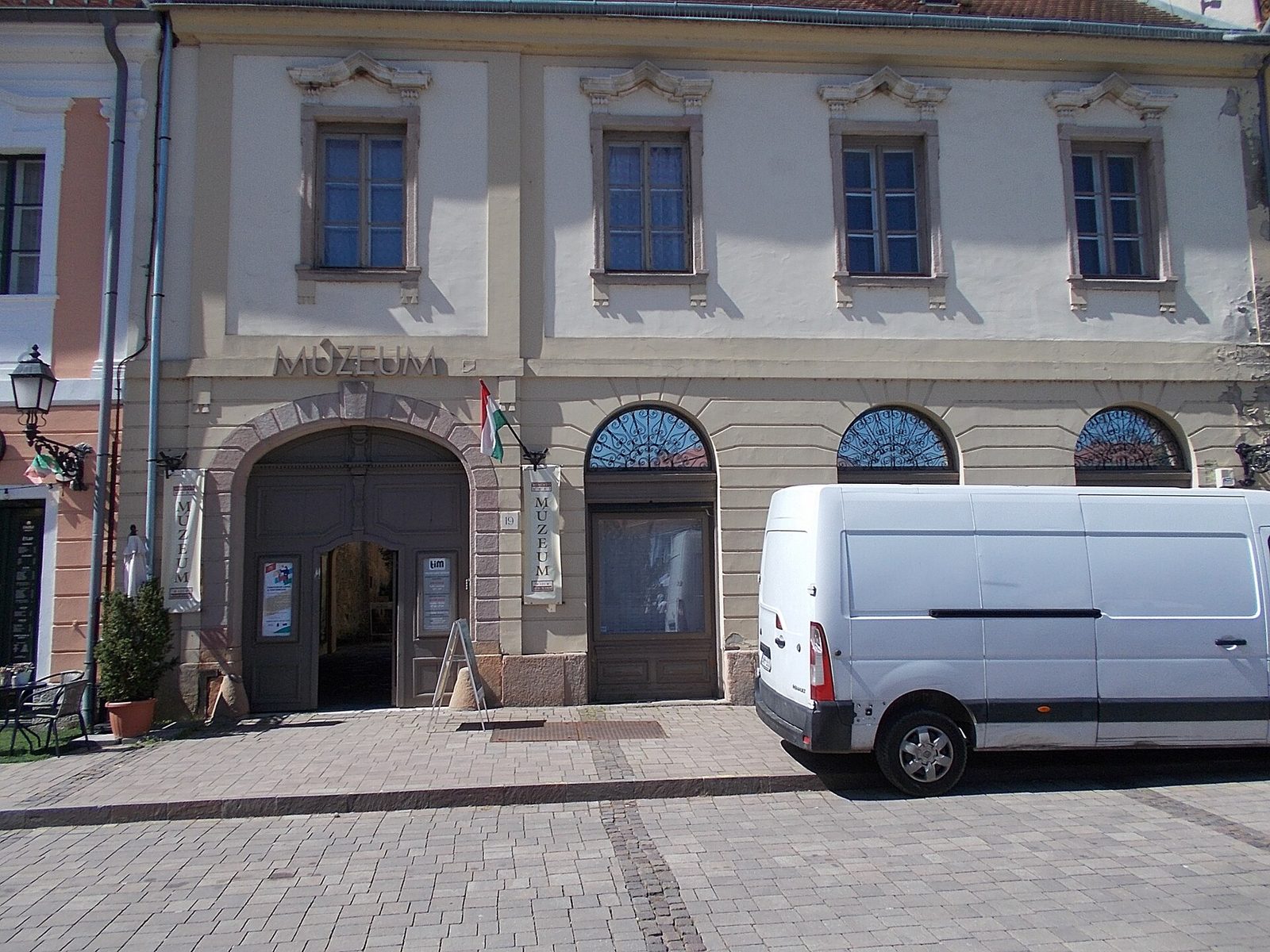 Kremowa barokowa kamienica przy Március 15. tér 19 w Vácu, z łukową bramą z napisem Múzeum i trzema łukowymi witrynami, siedziba wystawy Memento Mori