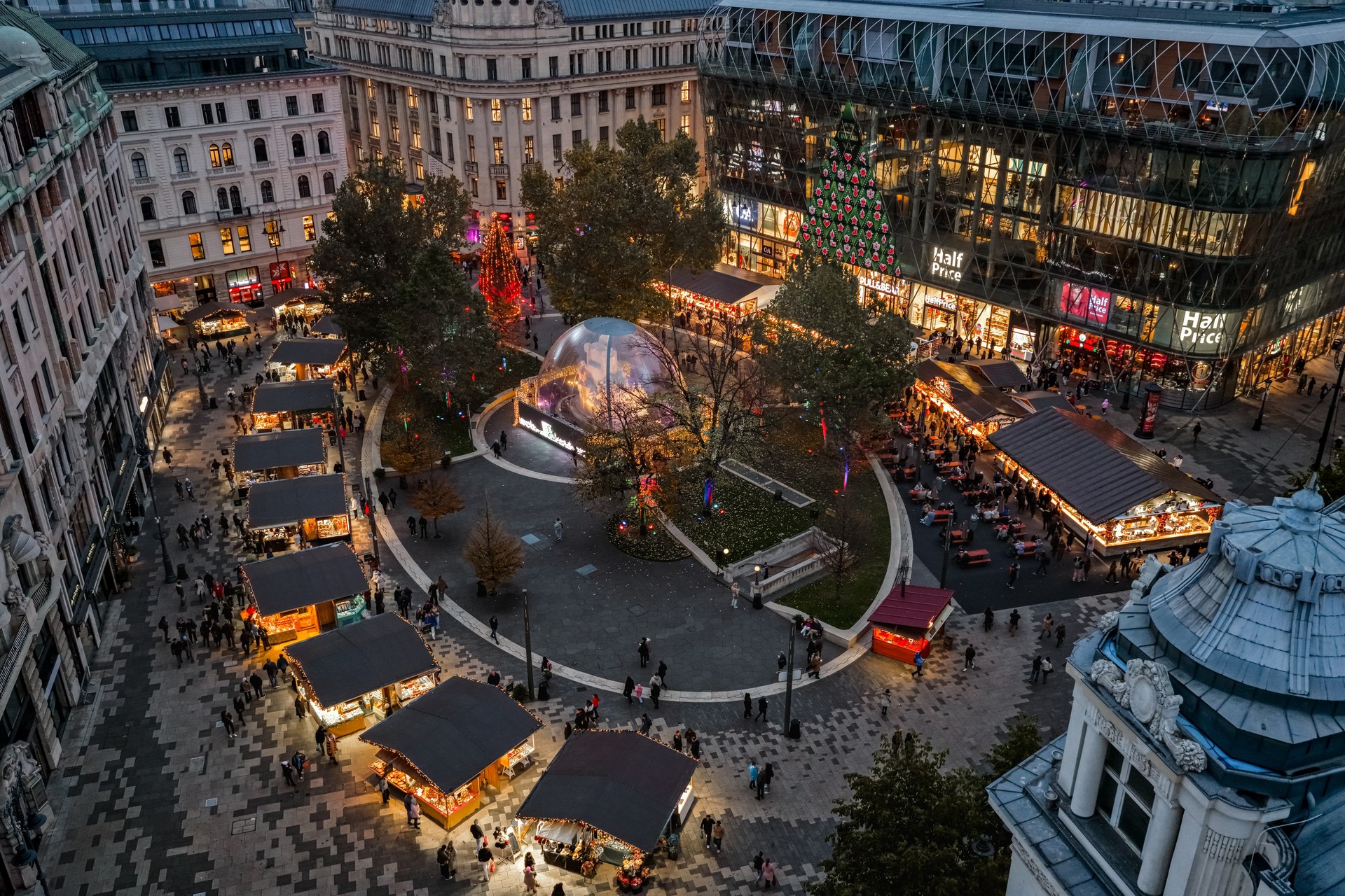 Vörösmarty tér during the 2025 Christmas market, seen from above at dusk, with wooden stalls around the square and lit Christmas trees